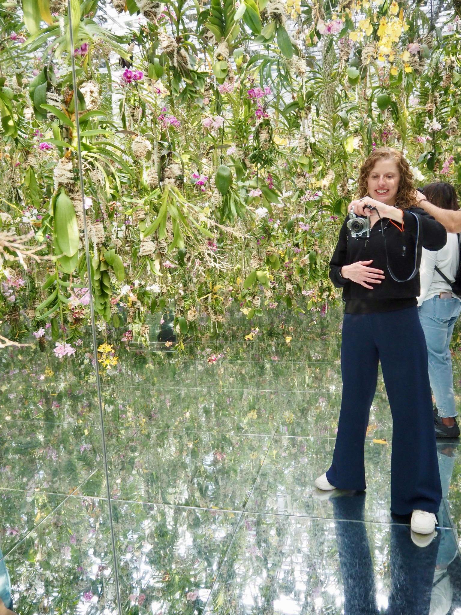 Elizabeth smiling with her camera in a room filled with orchids