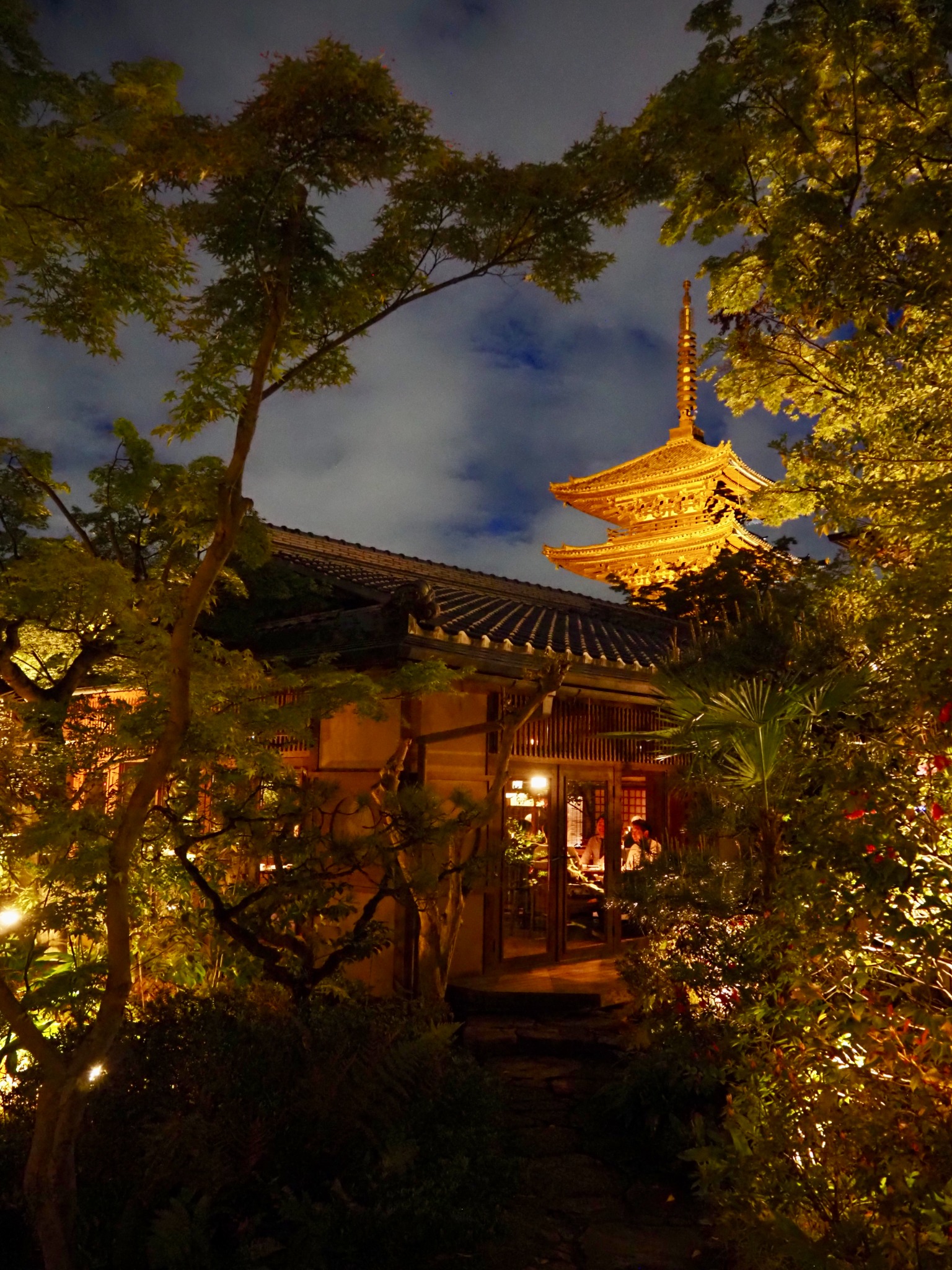 A glowing Kyoto pagoda framed by trees at night